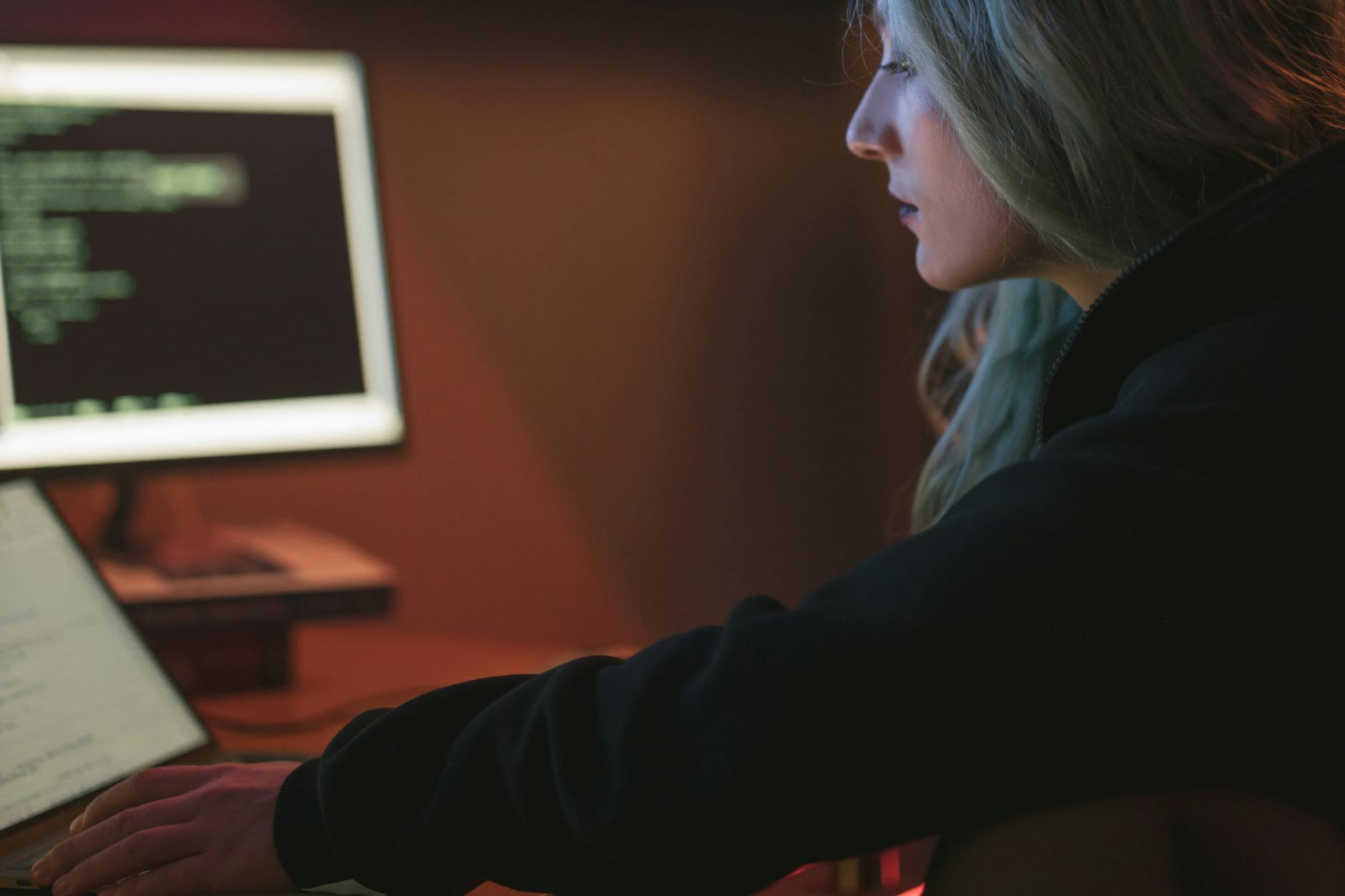 Programistka pracująca nocą przy laptopie z kodem w ciemnym biurze