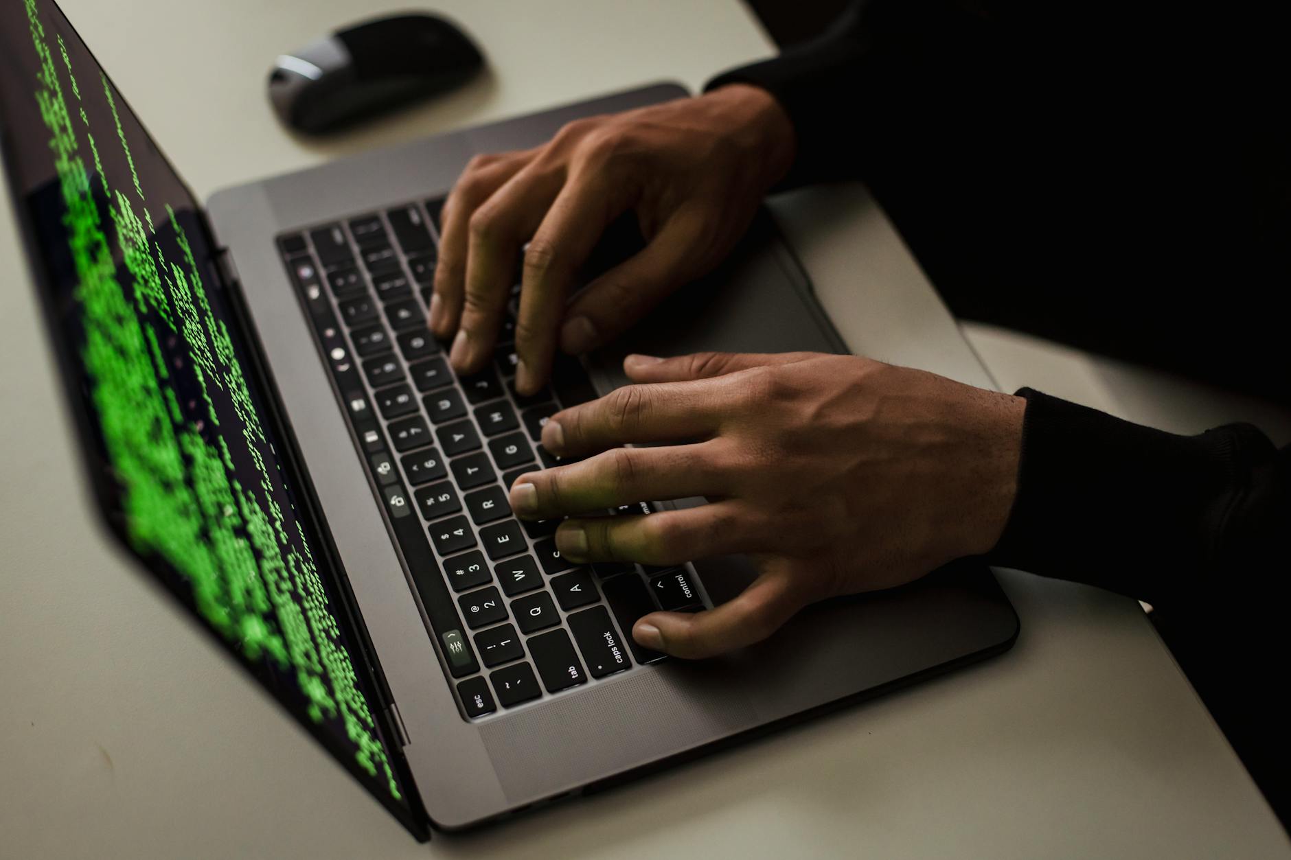 Haker przy biurku pisze na laptopie z danymi na ekranie