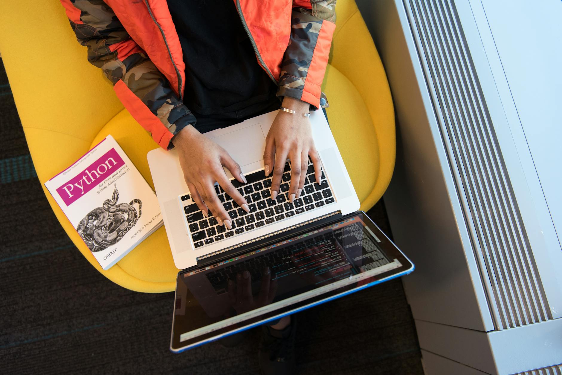 Kobieta programująca na laptopie, obok leży książka o Pythonie