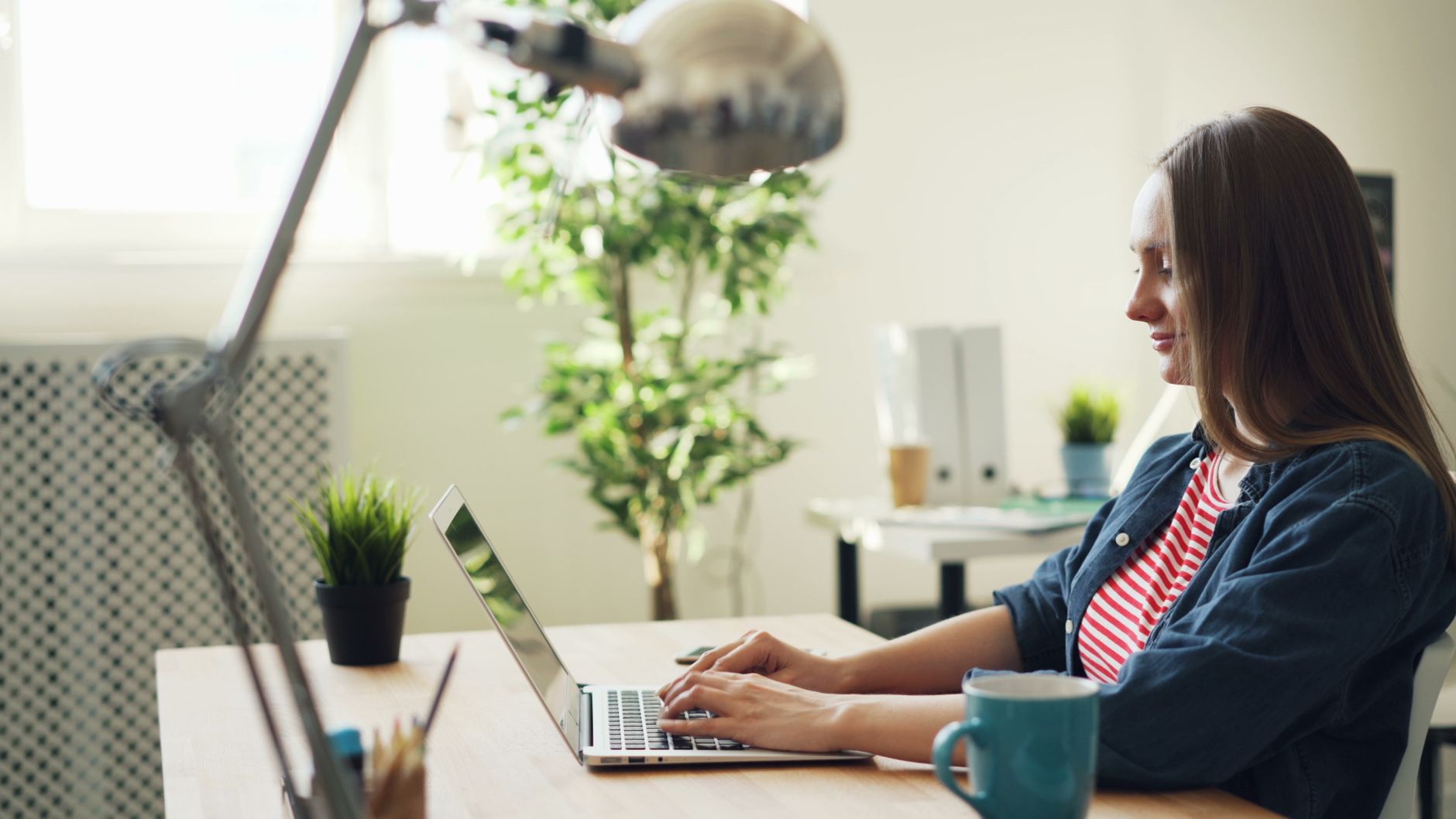 Uśmiechnięta kobieta pracuje na laptopie w nowoczesnym biurze z roślinami